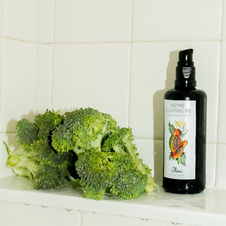 Image of the made safe certified enzyme cleansing oil in a shower next to a bunch of broccoli. broccoli is formulated in the enzyme cleansing oil as well as papaya enzymes and cucumber seed oil 